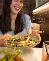 A promotional image for a Scottish restaurant in Glasgow, featuring a person presenting a fish dish to the camera.