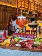 A promotional shot of a charcuterie board and two cocktails at a bar, featuring a warm, atmospheric interior setting.