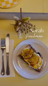A short, aesthetic montage showcasing 'Norah', an independent cafe located at Newhaven Pier in Edinburgh. The video features shots of the exterior, the scenic pier location, the interior decor, and various food and drink items like peach toast, sandwiches, and coffee.
