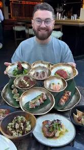 A creator reviews Gochu in Poynton, showcasing a variety of Japanese-inspired dishes including a large sushi platter, wagyu nigiri, and black cod. The video features the restaurant's interior and outdoor seating area, with the creator and a friend tasting and commenting on the food.