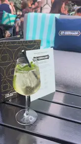 The video is a first-person vlog showcasing a St Germain Terrace Takeover at The Alchemist in Spinningfields, Manchester. The creator highlights the outdoor seating, the atmosphere with a live DJ, and samples various cocktails and canapes, including chicken strips and oyster-style shots.