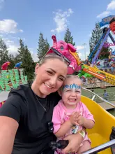 A selfie of a woman and a young child with face paint, taken on a fairground ride at the Trafford Centre. The image captures a candid, happy family moment against the backdrop of amusement rides.