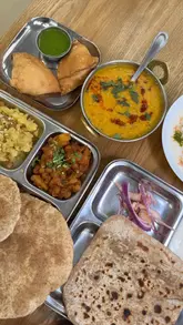 A montage of close-up shots featuring various Indian dishes including samosas, papri chaat, tadka daal, and paratha at Anand Sweets. The video focuses heavily on the texture and preparation of the food, with minimal shots of the venue itself.