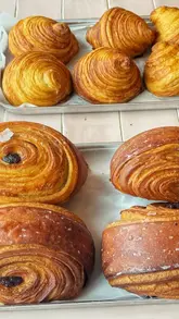 A short, engaging reel featuring a visit to Glaze Bakery in St Albans. The video highlights a variety of fresh pastries, including pain suisse and halva buns, alongside cookies and coffee. It features the creator sampling the food in an outdoor setting, providing a clear sense of the bakery's offerings and atmosphere.