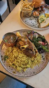 The video is a short, music-driven montage featuring a visit to Monaco Cafe. It highlights the interior, a variety of drinks, and specific dishes including lamb kabsa, a chicken burger with fries, and a baklava dessert. The creator is featured throughout, providing a personal touch to the venue tour.