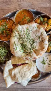 A promotional video for Tamatanga featuring a bottomless brunch experience. The creator showcases various Indian dishes including a cheese-filled naan, fish and chips, mutton roast, and a thali platter, alongside cocktails. The video uses quick cuts and close-up shots to highlight the food and the lively atmosphere of the venue.