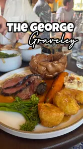 A video review of a Sunday roast experience at The George in Graveley, featuring close-ups of starters like cheese crumpets and crab donuts, followed by the main roast beef dinner, desserts, and drinks. The video includes shots of the pub's interior and outdoor garden area, accompanied by a voiceover review.
