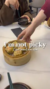 A short, handheld video capturing a table being filled with various bamboo steamers of dim sum, accompanied by a relatable text overlay about being 'not picky' as long as there is dim sum.