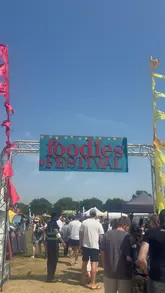 A montage of various food and drink items available at the Foodies Festival, including gyros, a burger, dumplings, ice cream, and various drinks, interspersed with shots of the festival grounds.