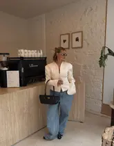 A stylish lifestyle shot featuring a woman holding a takeaway coffee in a modern, minimalist cafe setting. The image focuses on the aesthetic of the venue and the subject's outfit, using the coffee shop as a backdrop.