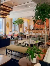 A high-quality, wide-angle interior shot of the UBA restaurant located within the Hart Shoreditch hotel. The image captures the sophisticated, warm-toned decor, featuring comfortable lounge seating, a well-stocked bar, and ambient lighting that creates an inviting and upscale atmosphere.