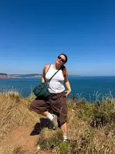 A lifestyle travel photo featuring a person posing on a coastal cliff path in Devon, capturing a sunny weekend outing.