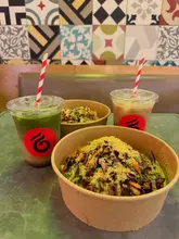A casual, top-down-angled shot of two takeaway bowls and two iced drinks on a table, likely in a cafe setting.