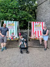 A family photo taken at Dudley Zoo & Castle featuring two adults and three children sitting on branded deckchairs in front of a stone wall. The image captures a casual day out, highlighting the venue's outdoor seating area and family-friendly atmosphere.