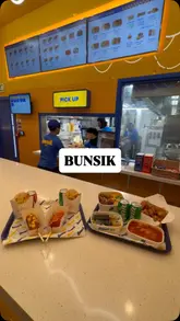 A fast-paced promotional video showcasing a variety of Korean street food dishes at a Bunsik location in the Trafford Centre, featuring corn dogs, kimbap, tteokbokki, and fried chicken.