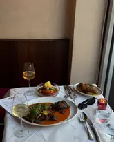 A high-quality, well-composed shot of a dinner table at a restaurant, featuring multiple dishes and glasses of wine. The lighting is soft and natural, highlighting the textures of the food and the clean table setting.