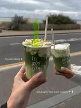 A first-person perspective shot of two matcha drinks being held up against a street background, promoting a matcha pop-up event.