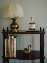 A high-quality, well-styled product shot of a bottle of Dewar's 21 Year Old Blended Scotch Whisky placed on a wooden shelf alongside decorative books and a brass swan ornament. The lighting is soft and even, creating an elegant, sophisticated atmosphere suitable for a premium spirits brand.