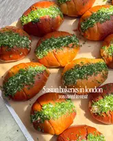 A high-angle, flat-lay photograph of several bread rolls filled with cream and topped with fresh chives, arranged on parchment paper. The image serves as a visual hook for a listicle about Asian bakeries in London.
