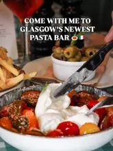 A high-quality, appetising close-up shot of a burrata dish being served, capturing the fresh texture of the cheese and the vibrant colours of the heritage tomatoes. The image effectively communicates the pasta bar experience with a busy, inviting table setting that includes sides and drinks, creating a sense of a shared, enjoyable meal.