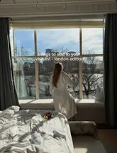 A lifestyle-focused shot taken from inside a hotel room, featuring a person in a bathrobe looking out of a large window at a river view, with a small plate of food on the bed in the foreground.