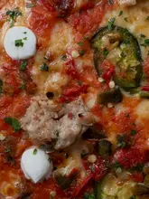A high-quality, extreme macro close-up shot of a pizza, focusing on the texture of the toppings including spicy sausage, ricotta, and jalapeños. The image is visually striking and highlights the quality of the ingredients.