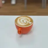 A high-quality, close-up shot of a latte with intricate tulip-style latte art served in a vibrant orange cup, set against a clean, neutral background.