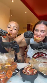 Two creators review a seafood boil restaurant, showcasing the variety of seafood, sides like mac and cheese balls and nachos, and the interactive, messy nature of the dining experience.