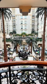 A high-quality promotional video showcasing an afternoon tea service held in a grand, glass-atrium hotel lobby filled with palm trees. The video features slow, cinematic pans of the venue, close-ups of the tea service including sandwiches, scones, and pastries, and a brief appearance of a guest enjoying the experience.