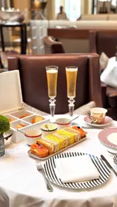 A montage showcasing an afternoon tea service at the Corinthia London, highlighting the elegant floral decor, the tiered serving stand, and the various pastries and sandwiches included in the experience.