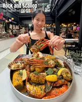 A high-quality, engaging shot of a creator presenting a large, abundant seafood boil platter in a market hall setting. The image effectively showcases the variety and freshness of the food, with the creator's smile adding a personal, welcoming touch.