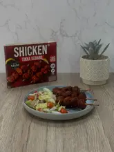 A static product shot featuring a box of SHICKEN Tikka Kebabs alongside a plate of the prepared food, consisting of skewers and a simple side salad.