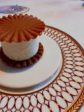 A high-quality, close-up shot of a 'Romeu e Julieta' dessert (guava and cheese sandwich) served on an elegant, patterned plate. The image captures the delicate, aerated texture of the cheese filling and the crisp, fluted edges of the biscuit, highlighting the refined presentation typical of a fine dining tasting menu.