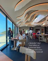 A high-quality, professional-looking shot of a restaurant interior in Cornwall, showcasing the venue's stunning coastal views and modern, elegant design. The image effectively communicates the upscale, serene atmosphere of the space.