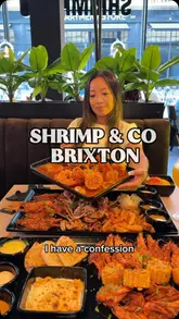 A creator reviews a seafood boil restaurant in Brixton, showcasing various platters featuring shrimp, crab, lobster, and sides like mac and cheese. The video focuses on the indulgent, hands-on experience of eating the food.