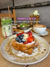 A bright and inviting food photography shot featuring a stack of French toast topped with fresh berries and granola, accompanied by a matcha latte, a coffee, and a shakshuka in the background, showcasing a cafe in Sowerby Bridge.