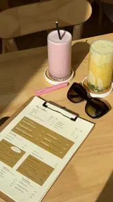 A short, aesthetic montage showcasing a cafe visit, featuring close-ups of wellness smoothies, pancakes, and poached eggs on sourdough. The video uses natural lighting and slow, deliberate cuts to highlight the food and the cafe's outdoor seating area.