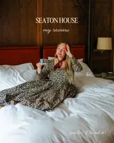 A high-quality, professional lifestyle shot featuring a creator sitting on a hotel bed at Seaton House in St Andrews. The image is well-composed, utilizing soft, natural lighting and a clean, inviting background that effectively conveys a sense of luxury and comfort.