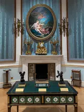 A high-quality, perfectly symmetrical photograph of an ornate display table and fireplace within the Wallace Collection, showcasing the historic interior and 18th-century art collection.