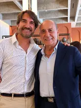 A high-quality portrait of two men posing together inside a sophisticated restaurant setting, likely captured during a celebratory event. The image features a clean, well-lit composition with a slightly blurred background that maintains the focus on the subjects.