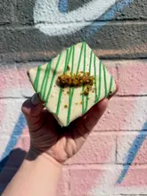 A close-up, handheld shot of a pistachio-topped brownie against a graffiti-covered brick wall, captured in Edinburgh.