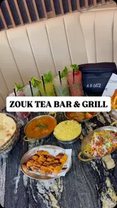 A promotional montage for Zouk Tea Bar & Grill, featuring shots of the restaurant exterior, interior, cocktail preparation, tandoor cooking, and a spread of various dishes and desserts.
