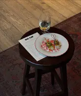 A moody, high-angle shot of a small table at Bar Flor, showcasing a plate of gilda-style pintxos and a glass of white wine, with the venue's menu placed alongside.