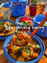 A vibrant, warm-toned shot of a homemade tofu panang curry being served, highlighting the texture of the dish and the aesthetic of the blue stoneware bowls.