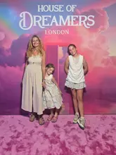A photograph of a woman and two children posing in front of a branded 'House of Dreamers' backdrop, likely taken during an immersive experience visit.