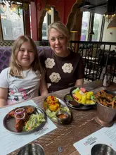 A candid, family-focused photograph taken at an Indian restaurant, showing a woman and a child at a table filled with various dishes, providing a relatable and authentic look at the dining experience.