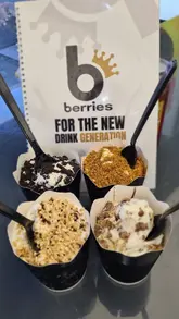A short, visually-focused montage showing the preparation of soft-serve ice cream desserts at Berries King of Shakes, featuring various toppings like sauces and crushed biscuits.