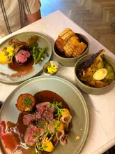 A high-quality, top-down shot of a contemporary Scottish dining spread, featuring plates of lamb, venison, hispi cabbage, and sourdough bread on a marble table.