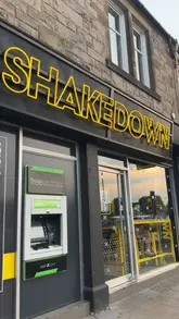 A short, music-led montage showcasing the exterior, menu board, and various food items from a burger restaurant called Shakedown. The video highlights burgers, fries, wings, and milkshakes.