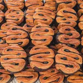 A high-quality, top-down close-up shot of multiple pain au chocolat pastries arranged in a repetitive pattern. The image highlights the intricate, flaky layers of the pastry and the dark chocolate filling, creating a visually satisfying texture-focused composition.